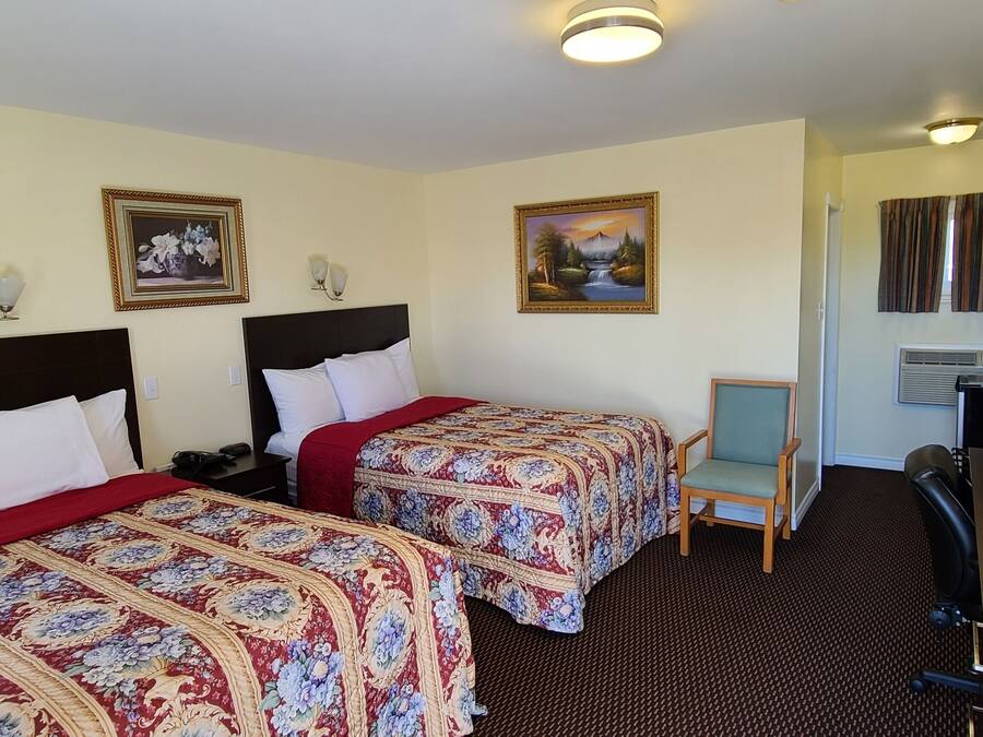 A hotel room with two beds, a desk, a chair, a TV, and a painting on the wall.