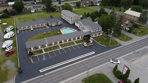 An aerial view of a motel with a swimming pool, multiple parking spaces, and a road in the foreground. - Fox Motor Inn (Greater Napanee)