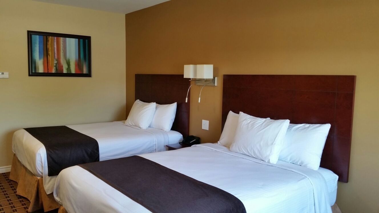 Dos camas con cabeceras marrones y ropa de cama blanca en una habitación de hotel.