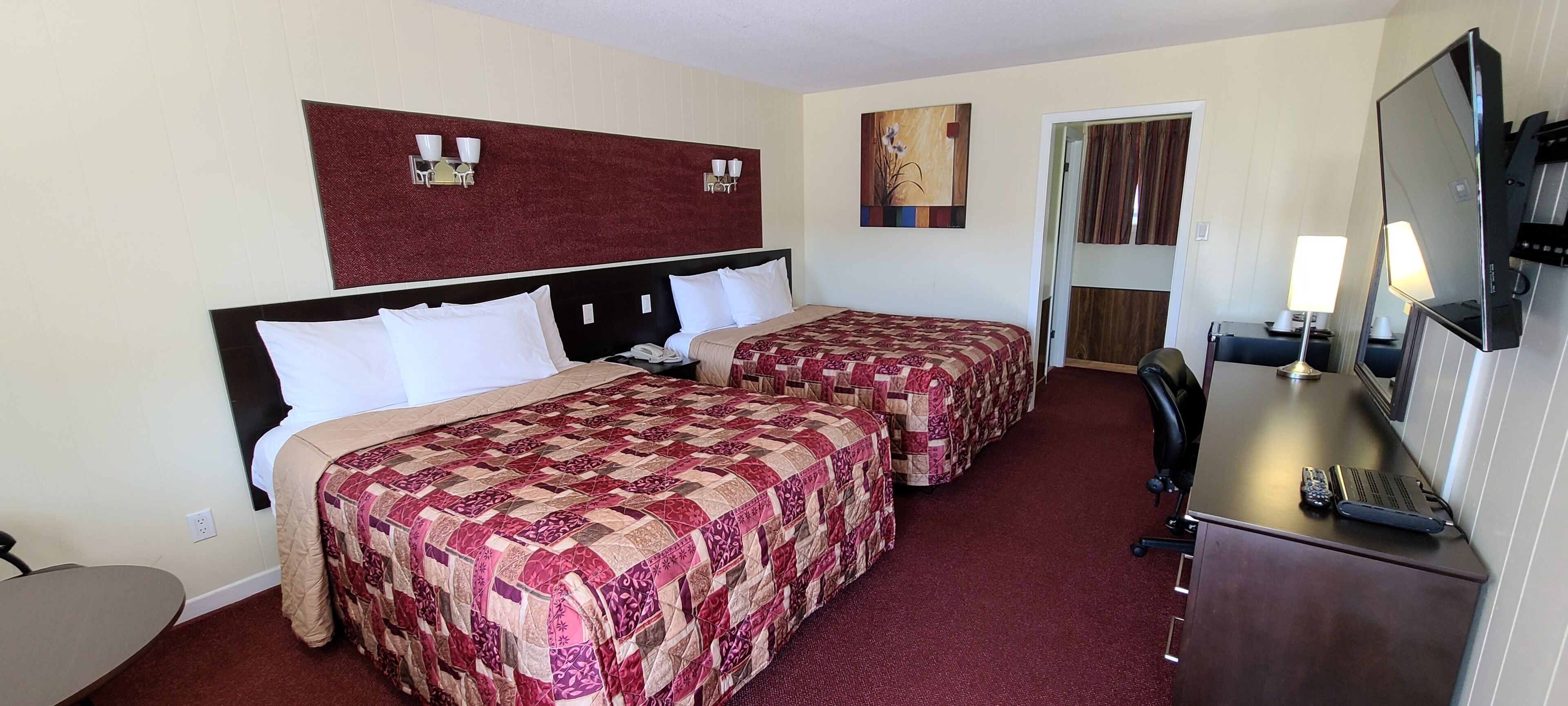 Een hotelkamer met twee bedden, een bureau, een stoel, een televisie en een schilderij aan de muur.