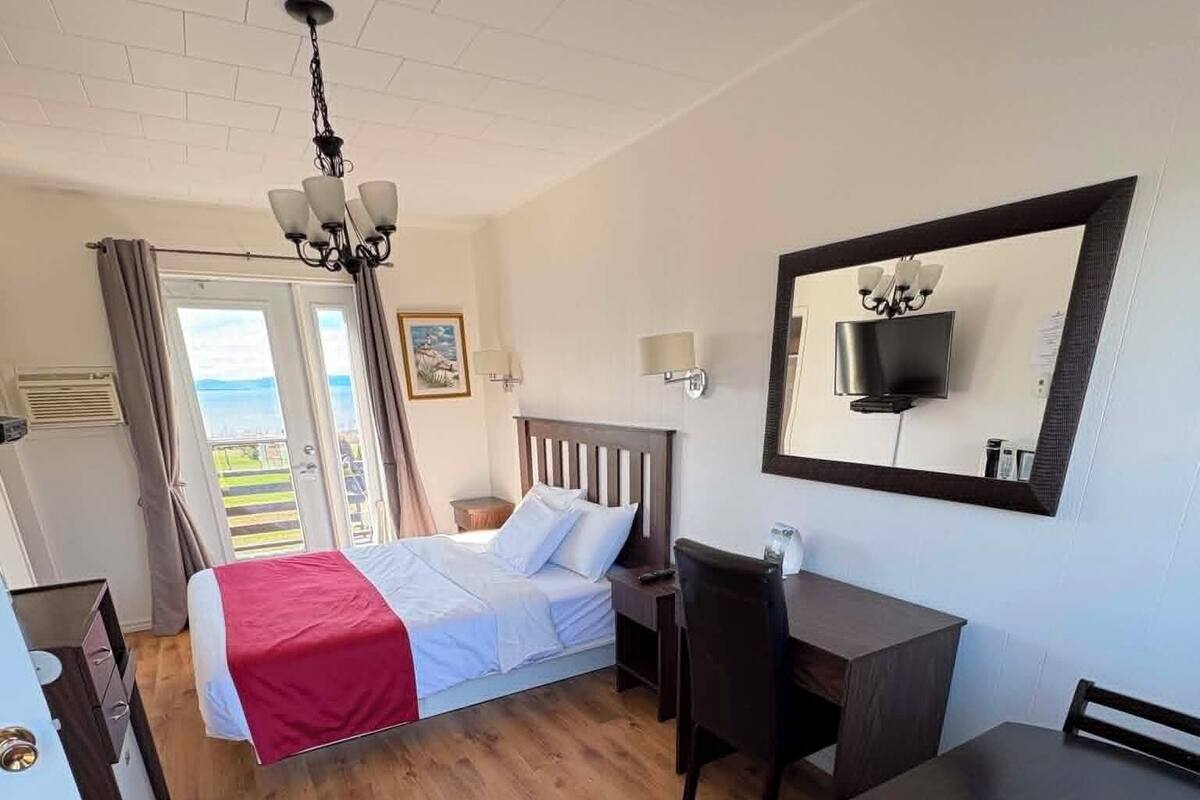 Habitación de hotel con cama, escritorio, silla, televisor y vistas al exterior.