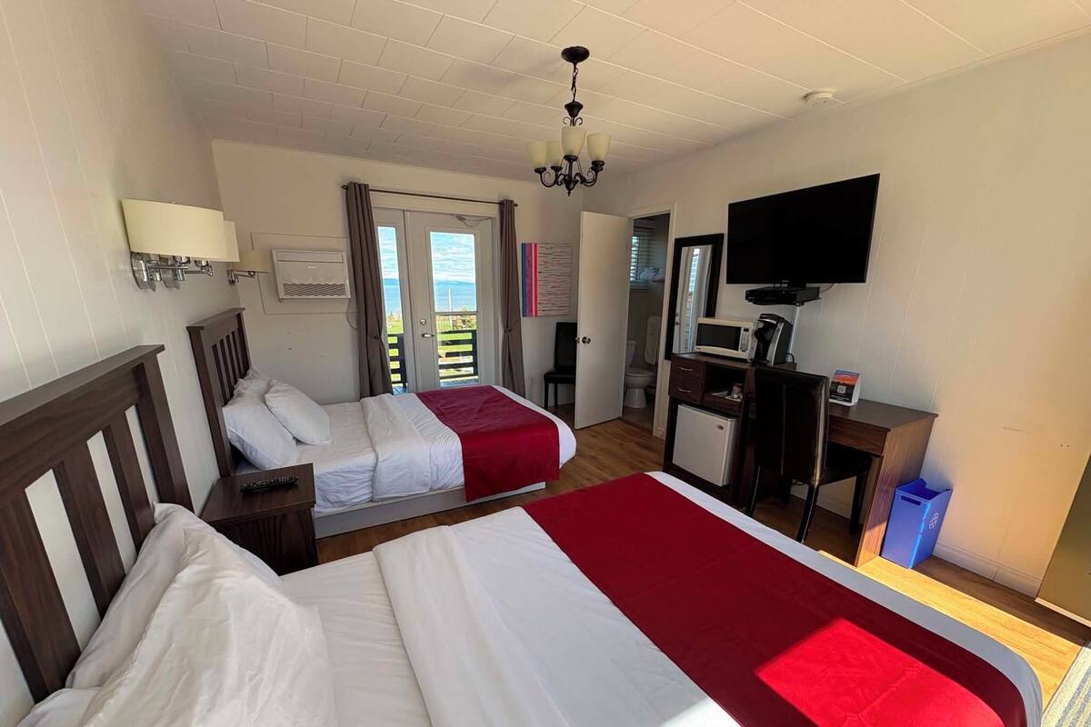 Habitación de hotel con dos camas, televisión, escritorio, microondas y refrigerador pequeño.