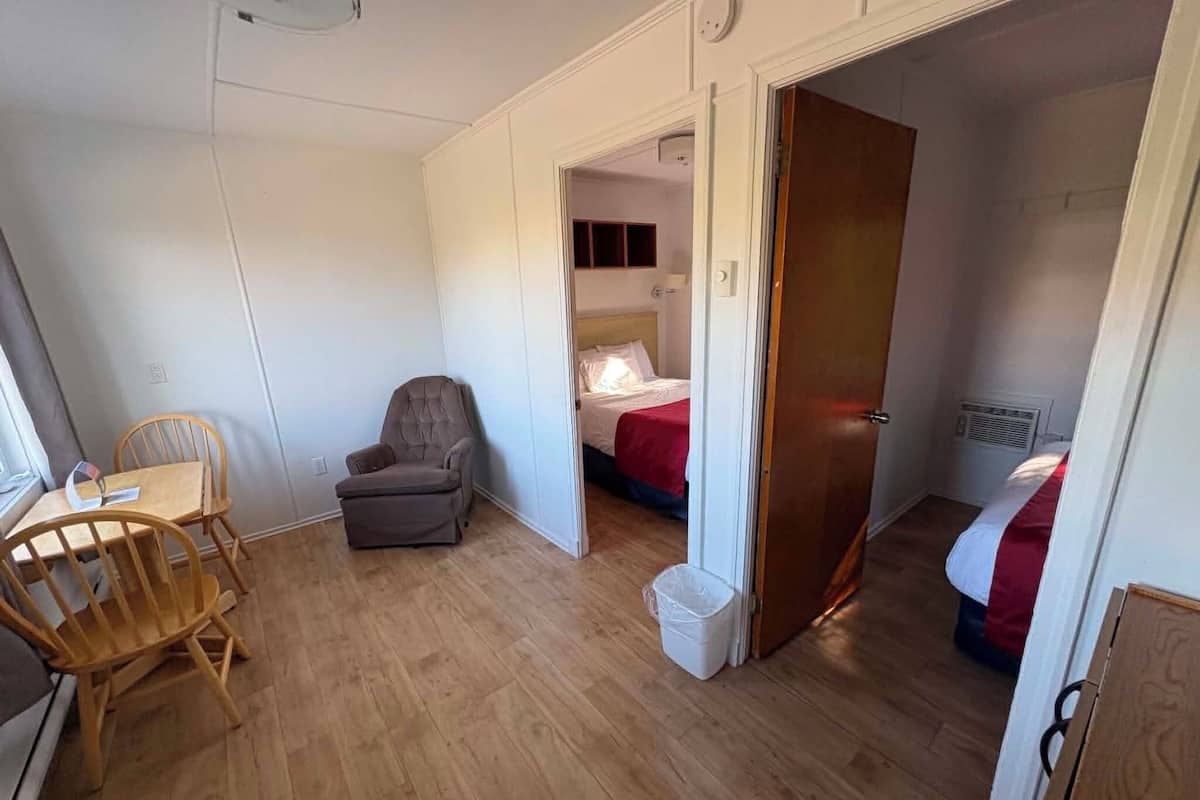 Una habitación pequeña y funcional con suelo de madera, una cama individual con una colcha roja, una silla y una mesa.