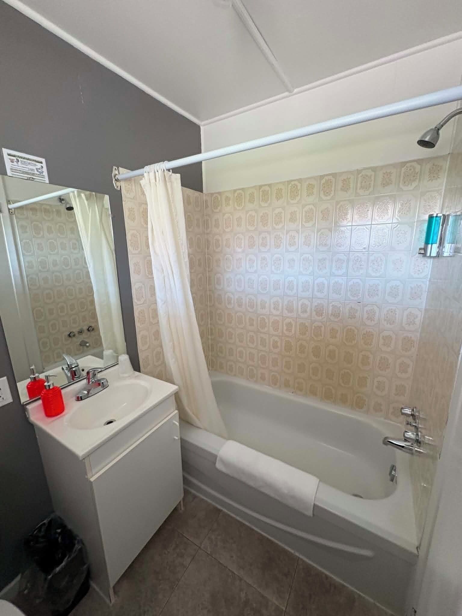 A bathroom with a bathtub, a sink, a mirror, and a shower curtain.