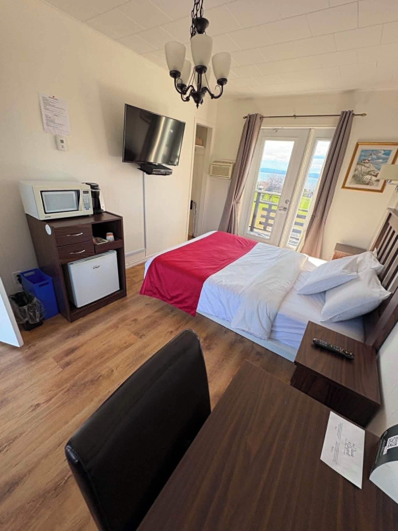 A hotel room with a bed, a desk with a chair, a television, a microwave, and a view of the outdoors.