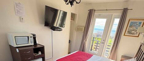 Habitación de hotel con cama, escritorio, silla, televisión, microondas y vista al exterior.
