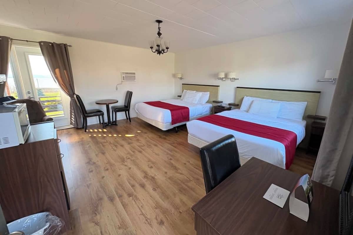 Habitación de hotel con dos camas, un escritorio, una silla, una mesita y vista al exterior.