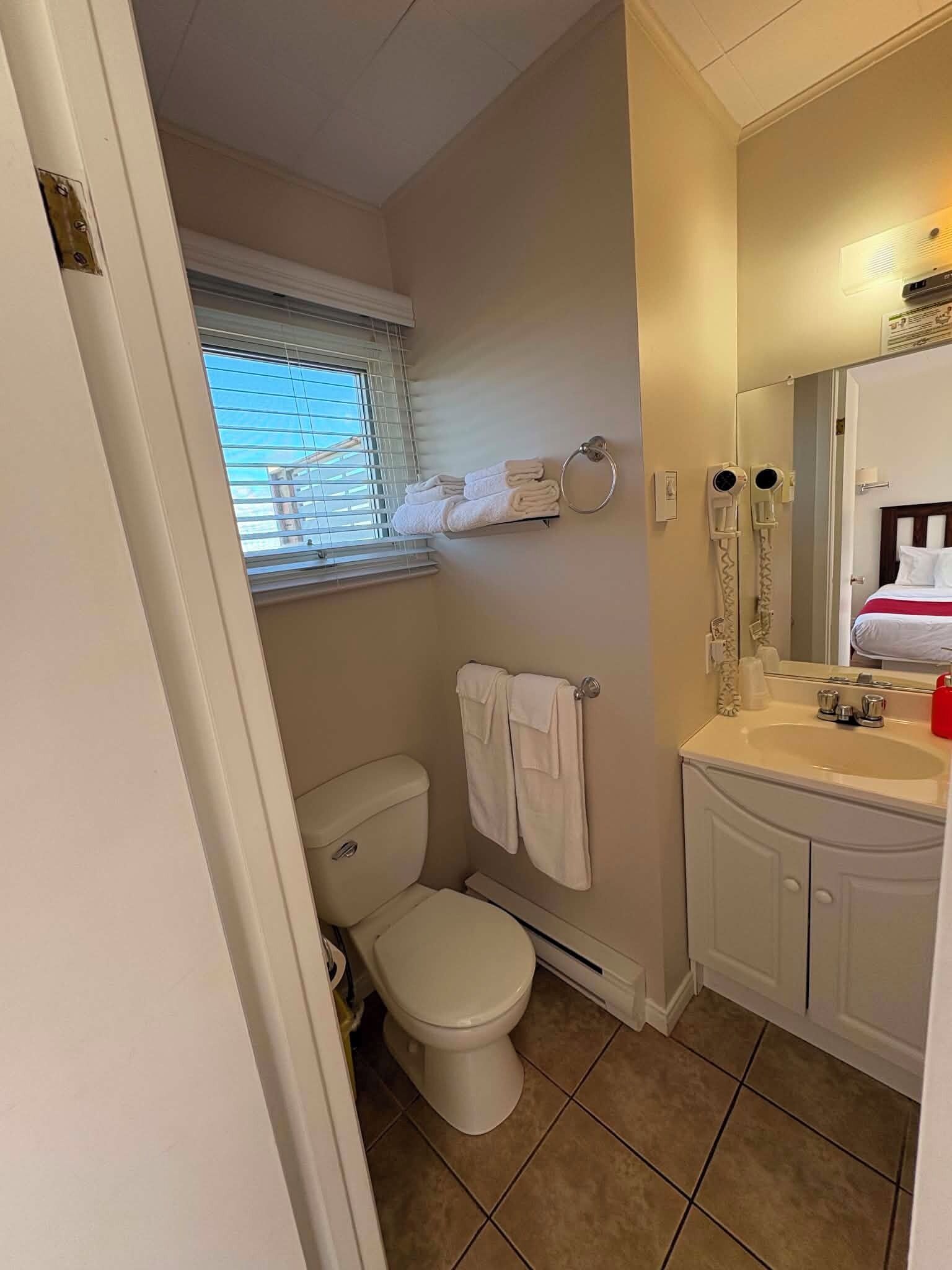 Un baño con inodoro, lavamanos, espejo y ventana.