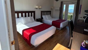 Quarto de hotel com duas camas, uma escrivaninha, uma cadeira e vista para o exterior.