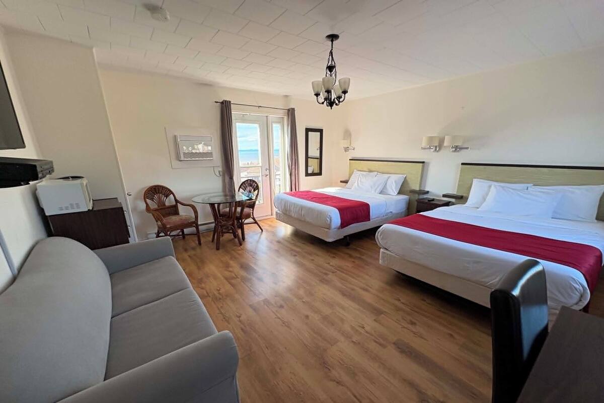 Habitación de hotel con dos camas, un sofá, una mesa de comedor con sillas, una araña y vistas al exterior.