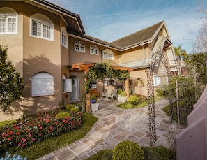 A house with a paved courtyard, a covered seating area, and a garden with flowers. - Pousada La Lavande (Gramado)