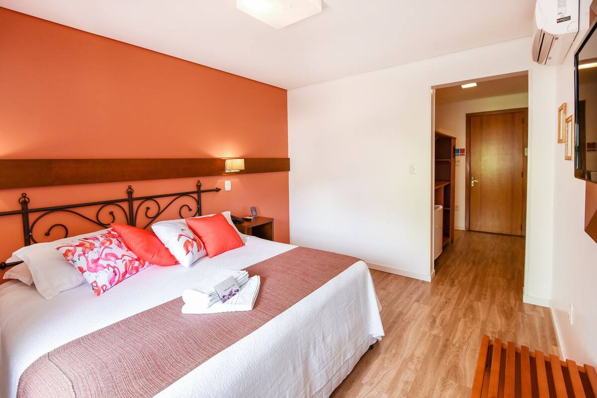 A neatly made bed with a white and pink bedspread, a wooden headboard, and a nightstand with a lamp.