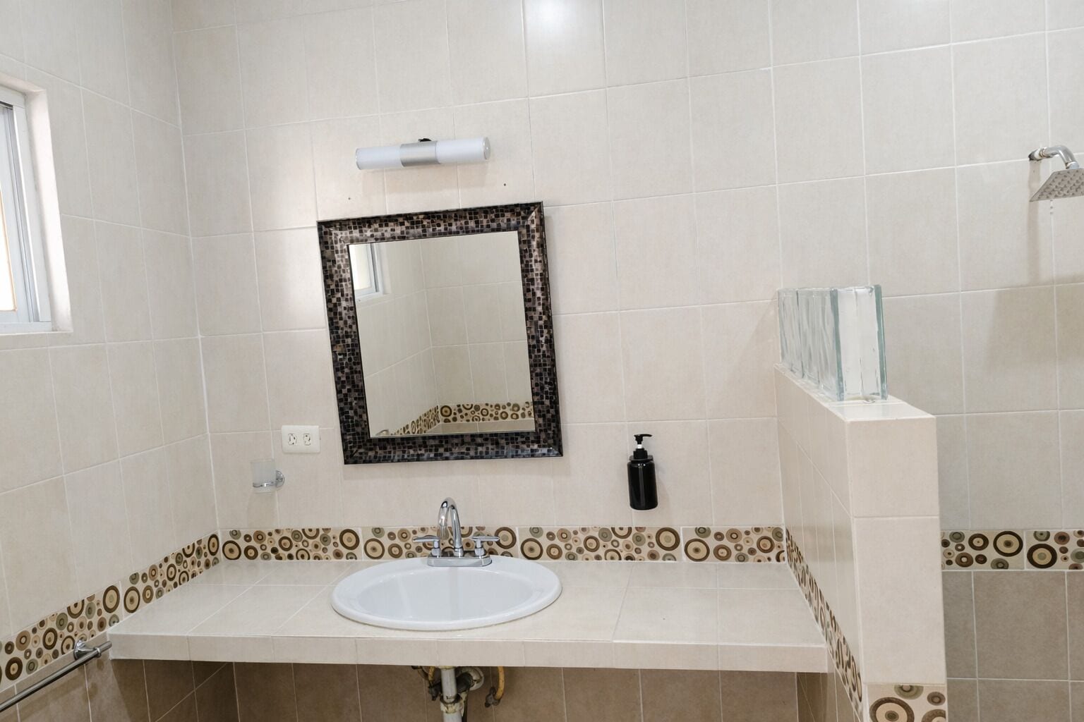 Un baño con un lavamanos blanco, un espejo con marco decorativo y baldosas estampadas en las paredes y el suelo.