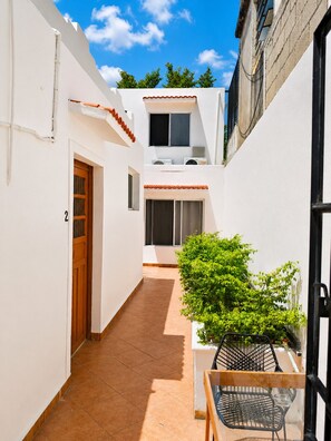 A narrow courtyard with a tiled floor, a wooden door, a small table with chairs, and a potted plant. - Guest House La Casa del Quetzal (Mérida)