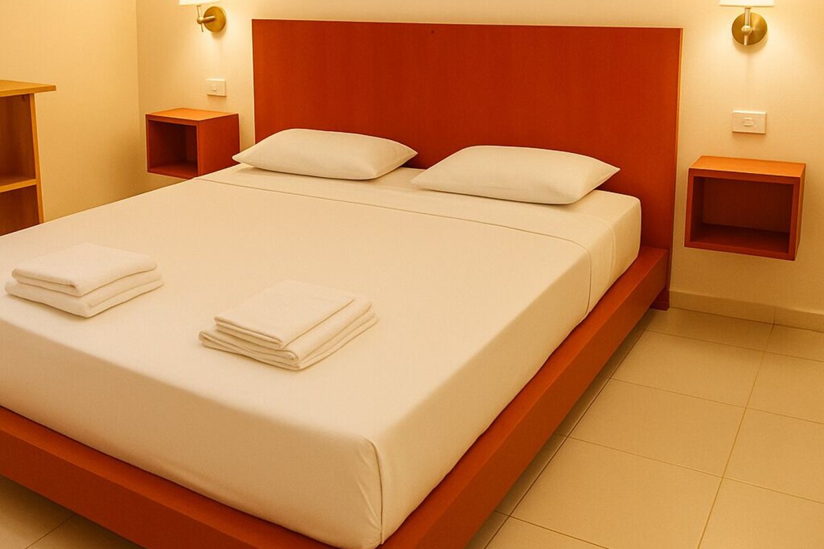 A hotel room with a large bed, two bedside tables, and wall-mounted lamps.