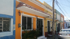 A residential building with a blue and orange facade, a gated entrance, and a parked car.