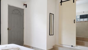 A hotel room with a bed, a door, a mirror, and a view of a tiled area.
