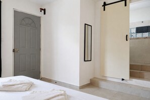 Habitación de hotel con cama, puerta, espejo y vista a una zona con baldosas.