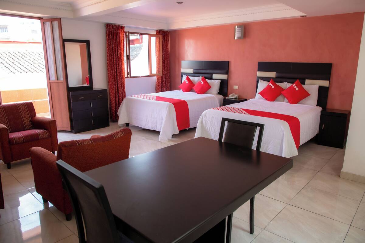 A hotel room with two beds, a dining table, chairs, a TV, and a wardrobe.