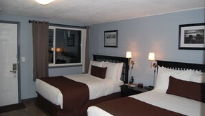 A hotel room with two beds, a window with curtains, a framed picture on the wall, and a nightstand with a lamp.