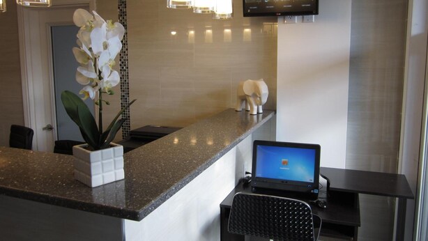 Zona de recepción de hotel con mostrador de mármol, una computadora portátil, un televisor montado en la pared y una orquídea en maceta.