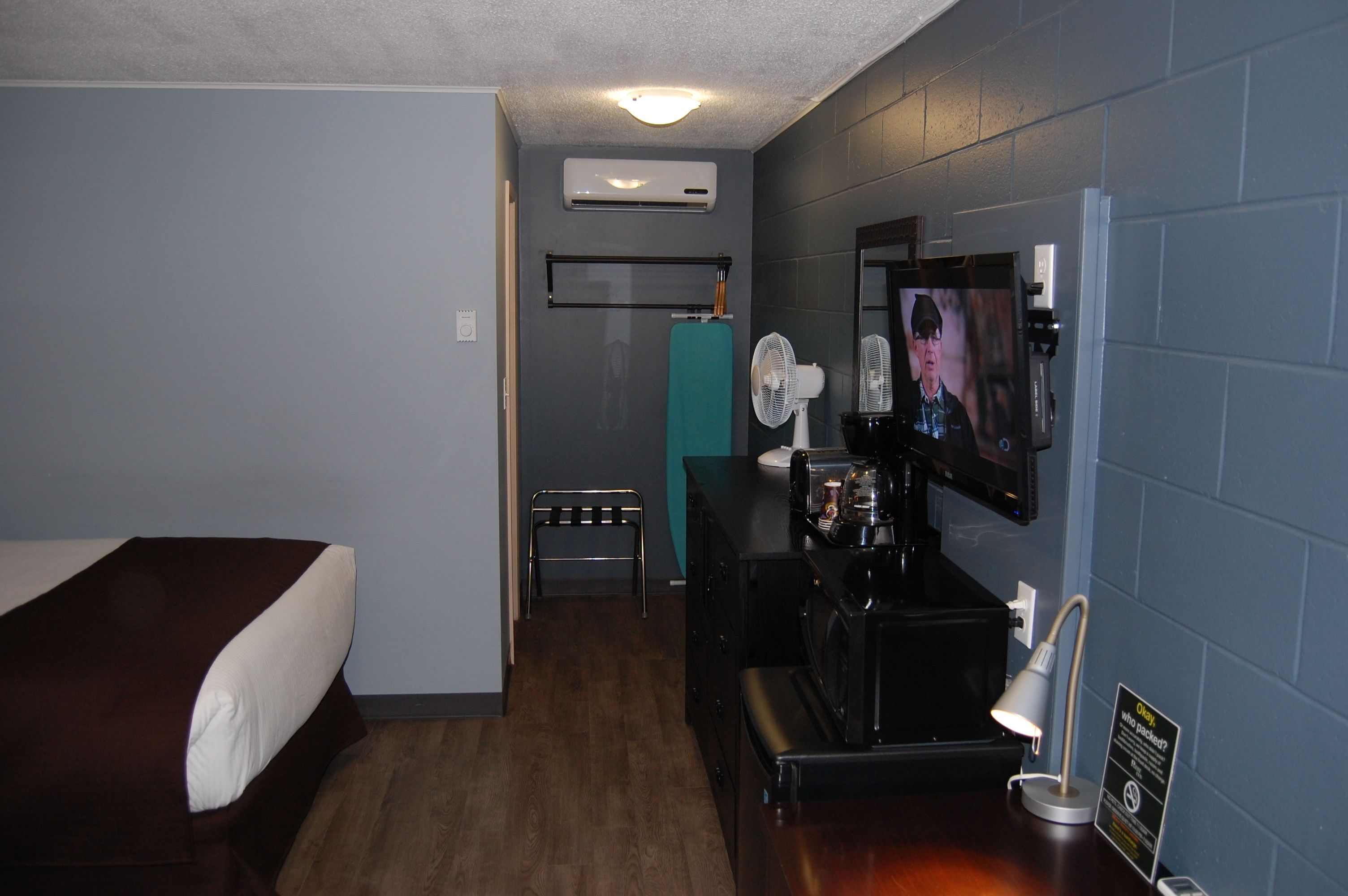 Habitación de hotel con una cama, un escritorio con computadora, un televisor, aire acondicionado y un ventilador.