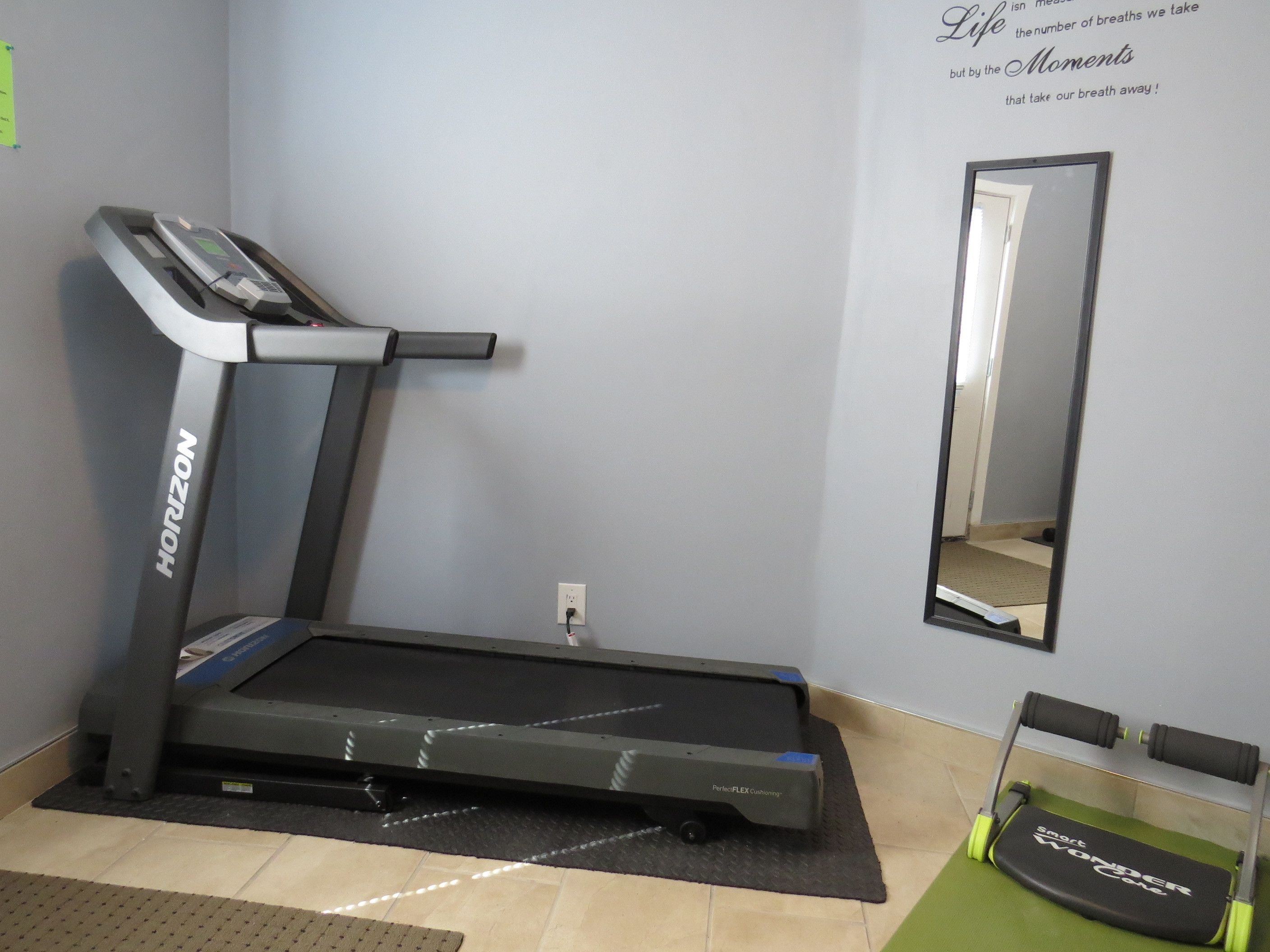 A treadmill in a room with a mirror and motivational quote on the wall.