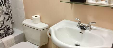 A bathroom with a toilet, sink, and glass shelf with toiletries.
