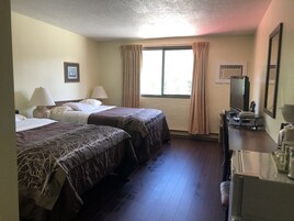 Una habitación de hotel con dos camas, un escritorio con espejo, televisión y ventana con cortinas.