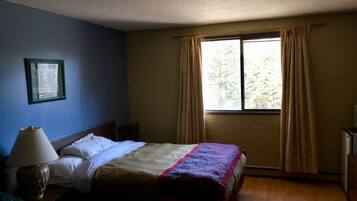 A hotel room with a bed, a nightstand, a lamp, a window with curtains, and a framed picture on the wall.