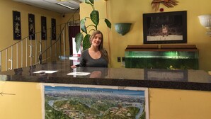 A reception desk with a map of West Kootenay & Boundary Country, a clock, and a plant. - Villager's Inn (Fruitvale)