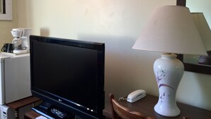 A television on a stand, a coffee maker, a lamp, and a telephone on a wooden table in a room with a plain wall. - Villager's Inn (Fruitvale)