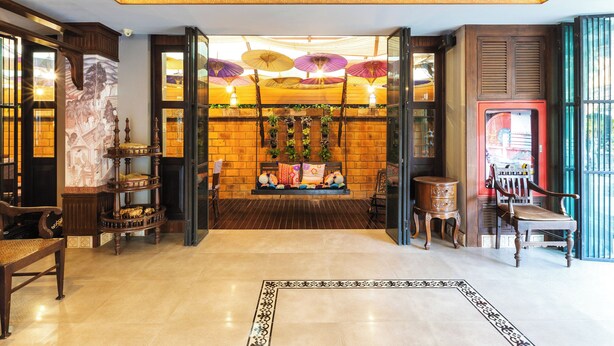 Een ruime lobby met een houten bank in klassieke stijl, een kleine tafel en een kamerbreed tapijt met patroon.