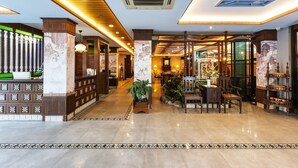 Een hotel lobby met een receptiebalie, een zithoek en decoratieve planten.