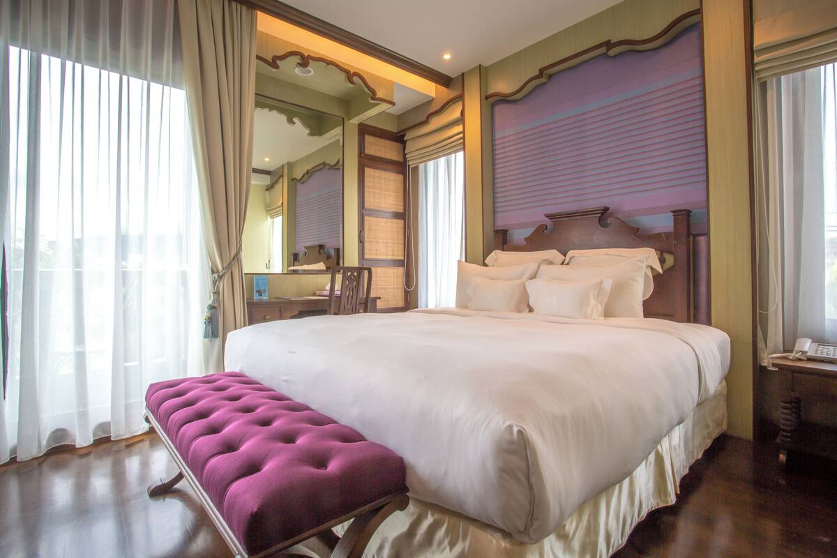 A large bed with a wooden headboard, a bench with a tufted backrest, and a bedside table with a telephone.