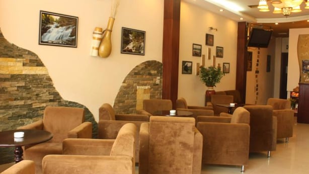 A lobby with sofas arranged in a U-shape, a stone wall, and several framed pictures on the wall. - Dalat Green City Hotel (Xuan Huong - Da Lat)