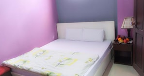 Una cama con una colcha estampada, una mesita de noche con una lámpara y una cesta de frutas.