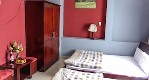 Ein Zimmer mit einem Bett, einem Holzschrank, einem kleinen Tisch mit Blumenvase und einer Lampe.