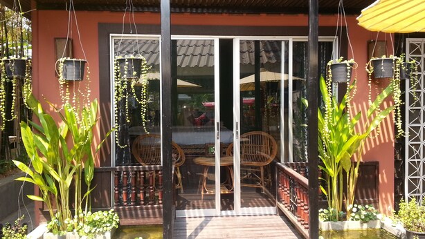A covered outdoor area with a wooden deck, potted plants, and a glass door entrance. - Sirikamsan House (Chiang Mai)