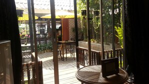 A room with a sliding glass door leading to an outdoor area with a table and chairs, a small TV on a table, and a view of the street and greenery outside. - Sirikamsan House (Chiang Mai)