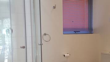 Un baño con cabina de ducha de vidrio, inodoro, bidé y ventana con persianas.