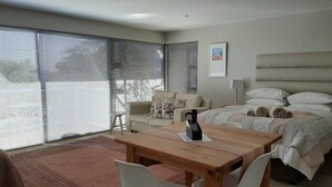 A modern bedroom with a large bed, a bedside table, a chair, and a window with blinds.