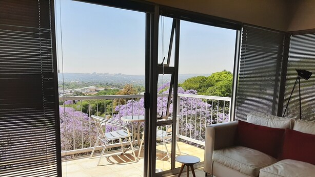 A balcony with a view of purple flowers and a distant cityscape.