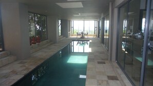 A modern indoor pool area with a glass wall on one side and a view of the outdoors.