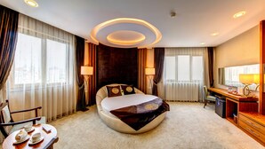 Habitación de hotel moderna con una cama grande, un escritorio con silla, un televisor y vistas a la ciudad a través de las ventanas.