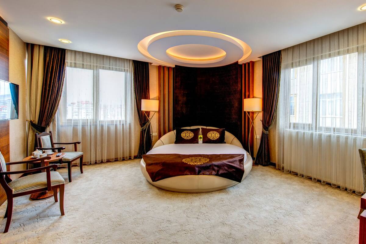 Habitación de hotel con una cama grande, dos lámparas de noche, un escritorio con una silla y vistas a la ciudad a través de amplias ventanas.
