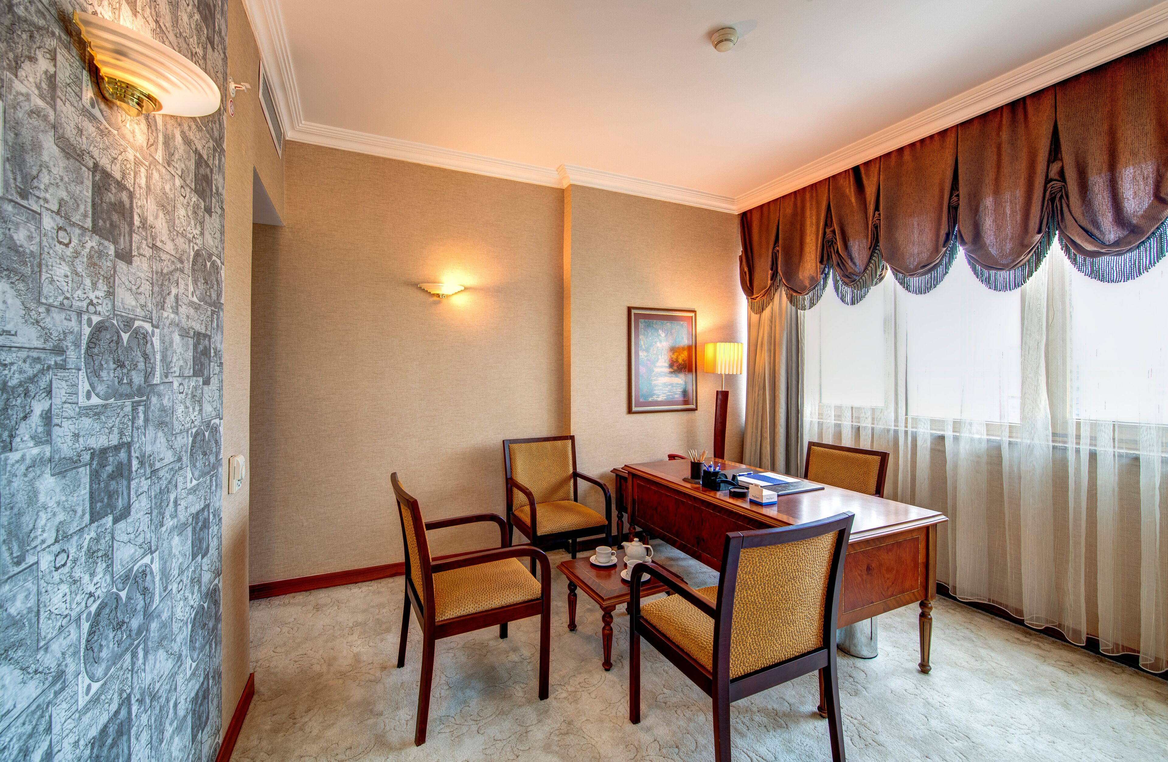 A hotel room with a stone wall, a dining table with four chairs, a lamp, and a painting on the wall.