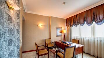 A hotel room with a stone wall, a dining table with four chairs, a lamp, and a painting on the wall.