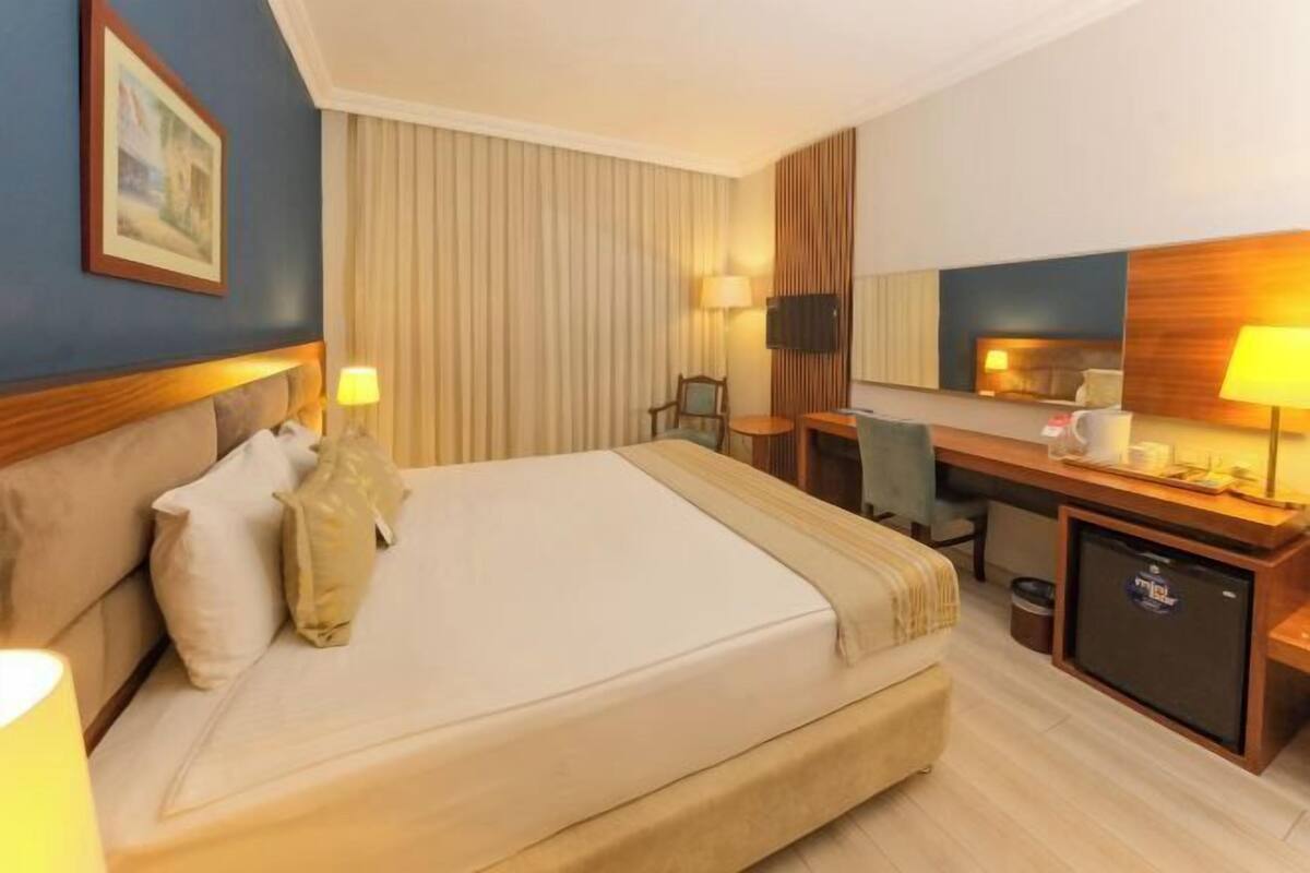 Una habitación de hotel con cama, mesita de noche, lámpara, escritorio, silla y televisor.