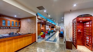 Un vestíbulo de hotel con mostrador de recepción, cabina telefónica y zonas de estar coloridas.
